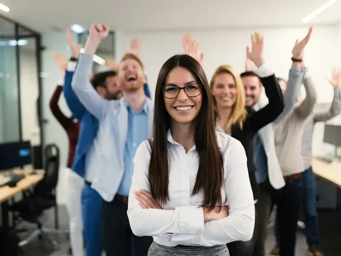 Smiling team with a confident leader in a bright office, coworkers cheering to celebrate growth and listings